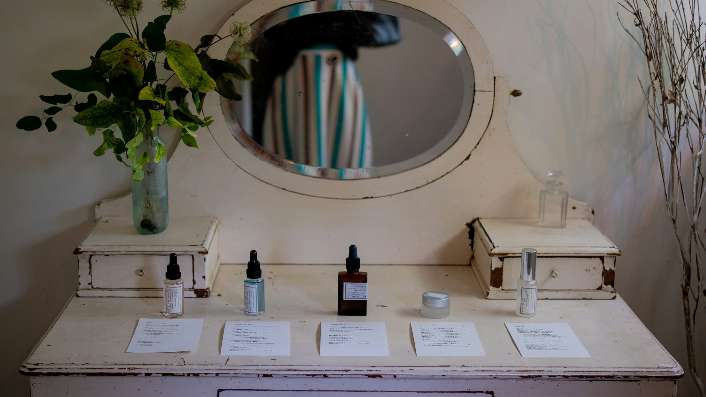 Skincare products arranged in a row on a white vanity table, a round mirror behind them.